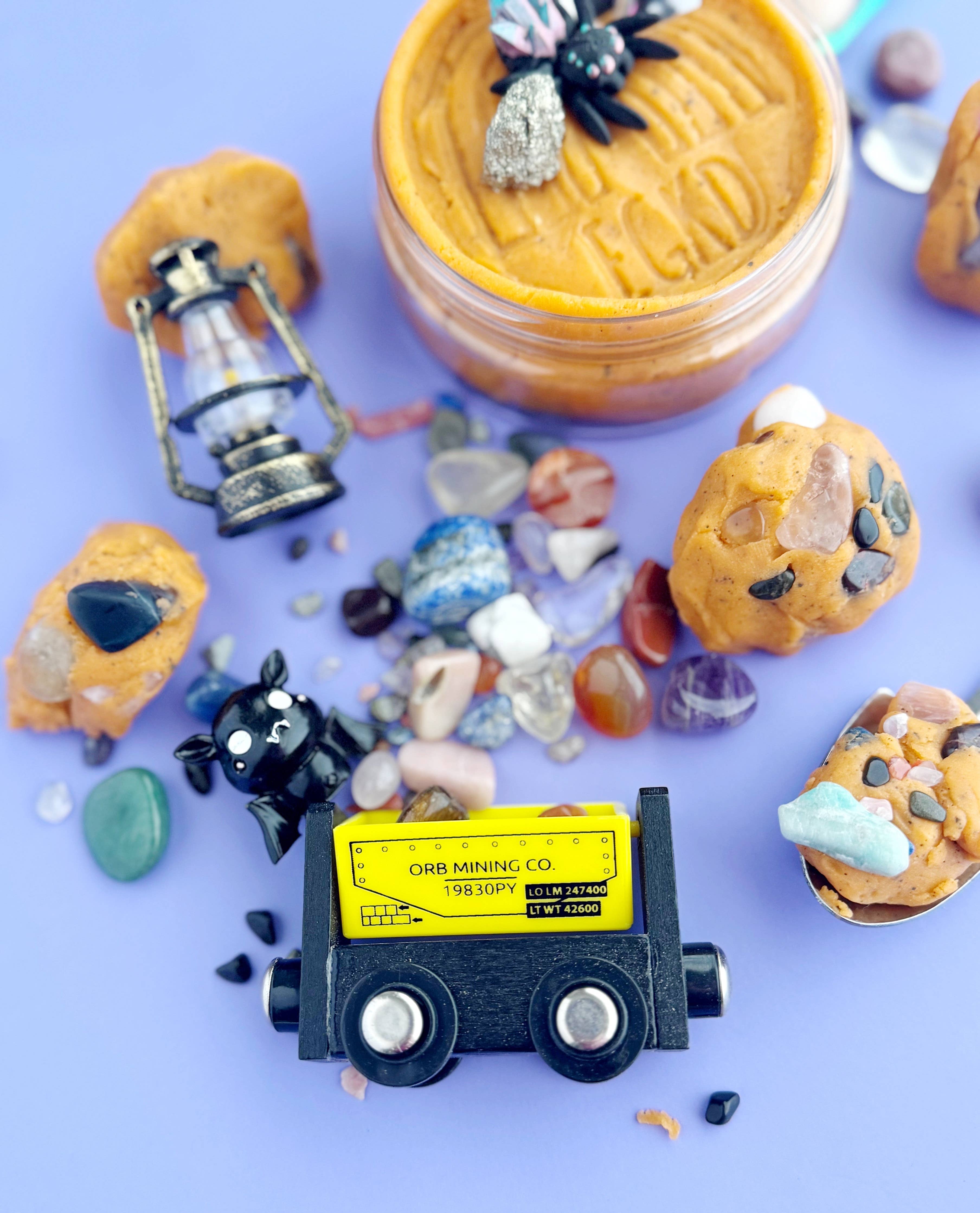 Miniature mining truck surrounded by small rocks and a jar of what appears to be peanut butter on a purple background.