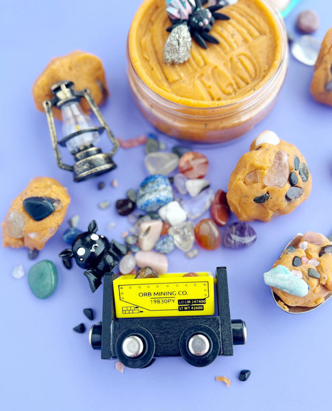 Miniature mining truck surrounded by small rocks and a jar of what appears to be peanut butter on a purple background.