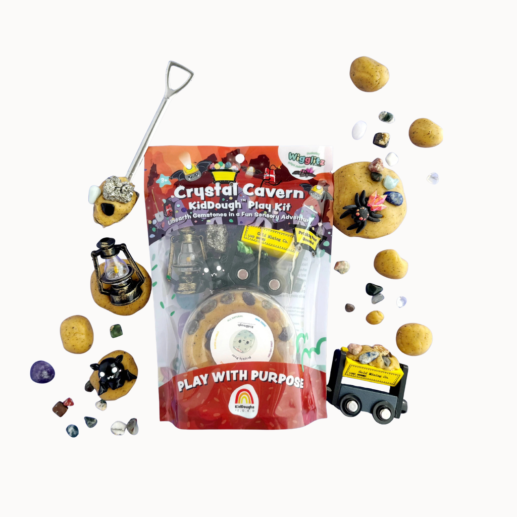 Crystal Cavern KidDough Play Kit in its clear plastic packaging, surrounded by themed play pieces including miniature rocks, a small shovel, a lantern, a toy cart, and loose colored stones on a plain white background.