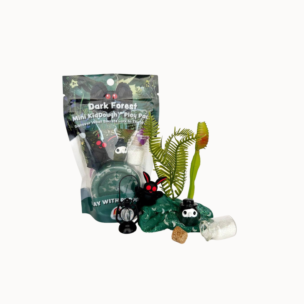 A dark forest-themed mini kid's play set in its clear packaging, displayed with its contents including small black and white monster figures, green ferns, a red flower, and a small clear bottle on a white background.