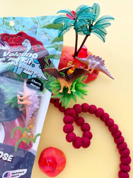 Toy volcano with palm trees, red beads, and a toy dinosaur on a yellow background