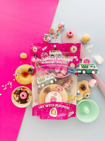Doughnut-themed play kit packaging on a pink and gray background with donut decorations.