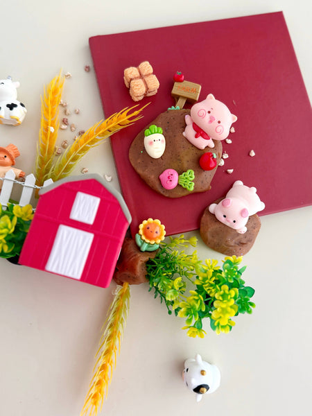 Decorative cookies shaped like farm animals and a barn on a red book with plants and a cow figurine.