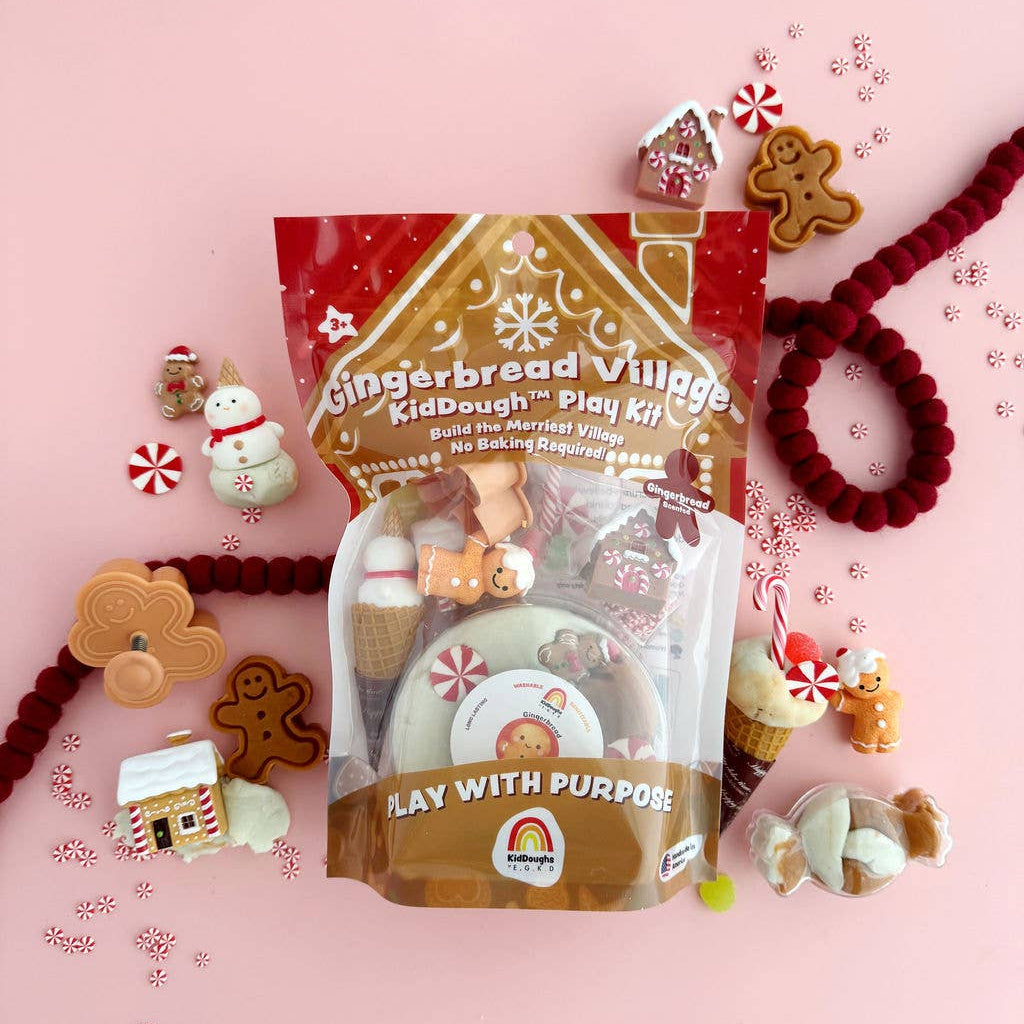 Gingerbread Village kid dough play kit on a pink background with gingerbread cookies and candy decorations.
