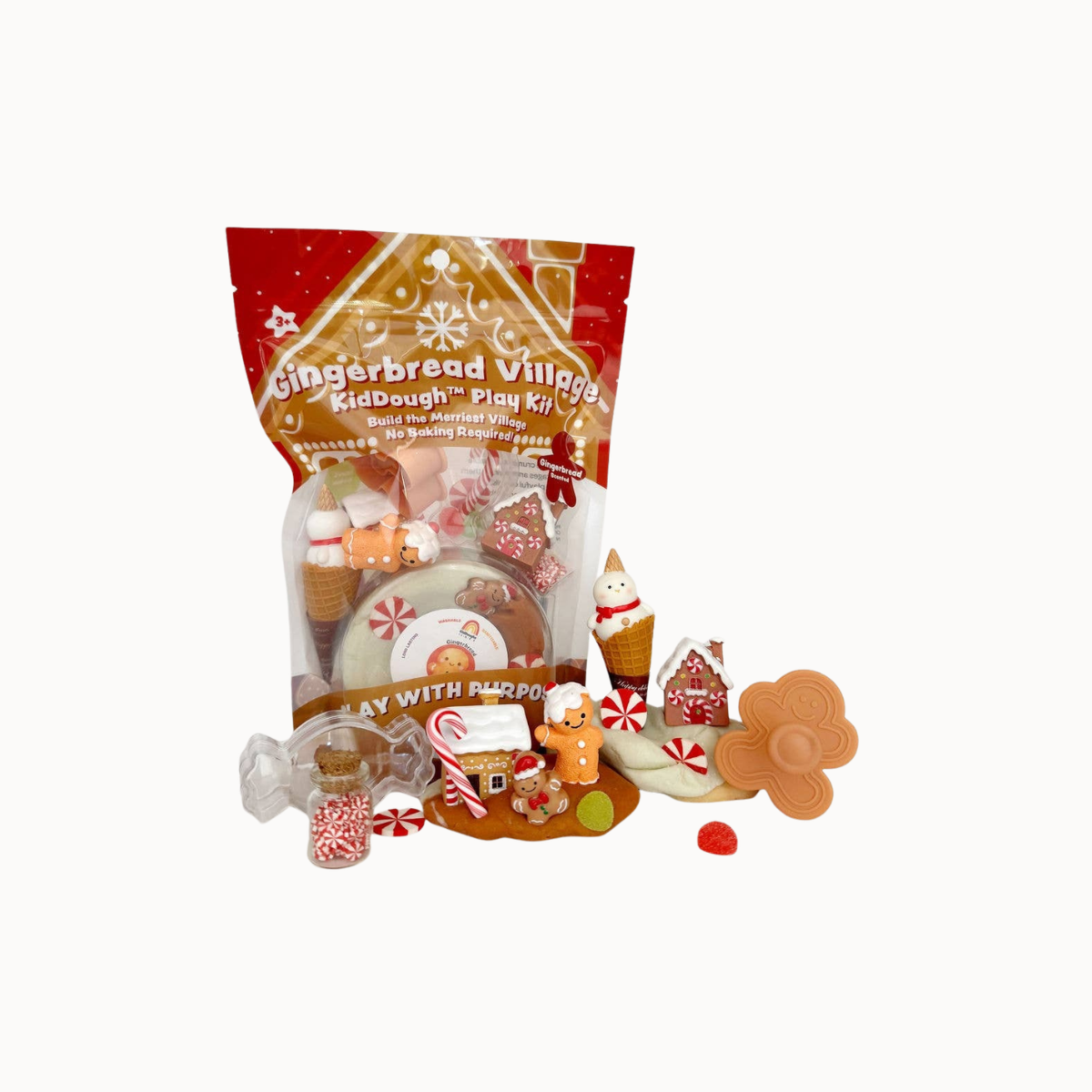 Gingerbread Village KidDough Play Kit in a red and gold stand-up pouch, shown with assorted gingerbread-themed play pieces and candies arranged in front on a plain white background.
