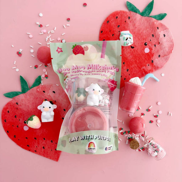 Pink toy with a cow design, strawberry-shaped packaging, and decorative elements on a pink background.