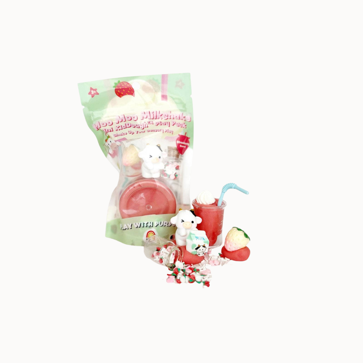 A packaged toy set featuring a small white bear figurine, a red milkshake with a blue straw, strawberry-themed accessories, and candy pieces, displayed in front of a clear plastic bag with pastel green and pink packaging on a white background.