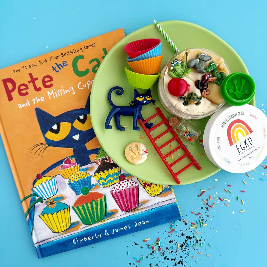 A styled flat-lay featuring the children's book 'Pete the Cat and the Missing Cupcakes' next to a green plate with themed cupcake decorations, a small red ladder, a blue cat figurine, and a container labeled 'Cupcake Party' by EG&LD, all arranged on a bright blue background with scattered confetti.