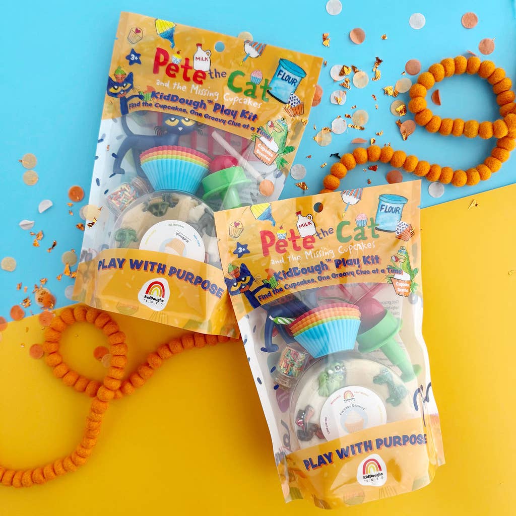 Two packages of Pete the Cat KidDough Play Kit arranged on a bright blue and yellow background with orange beaded loops and confetti scattered around. The packages are clear plastic with yellow-orange labels and show the dough play set inside.