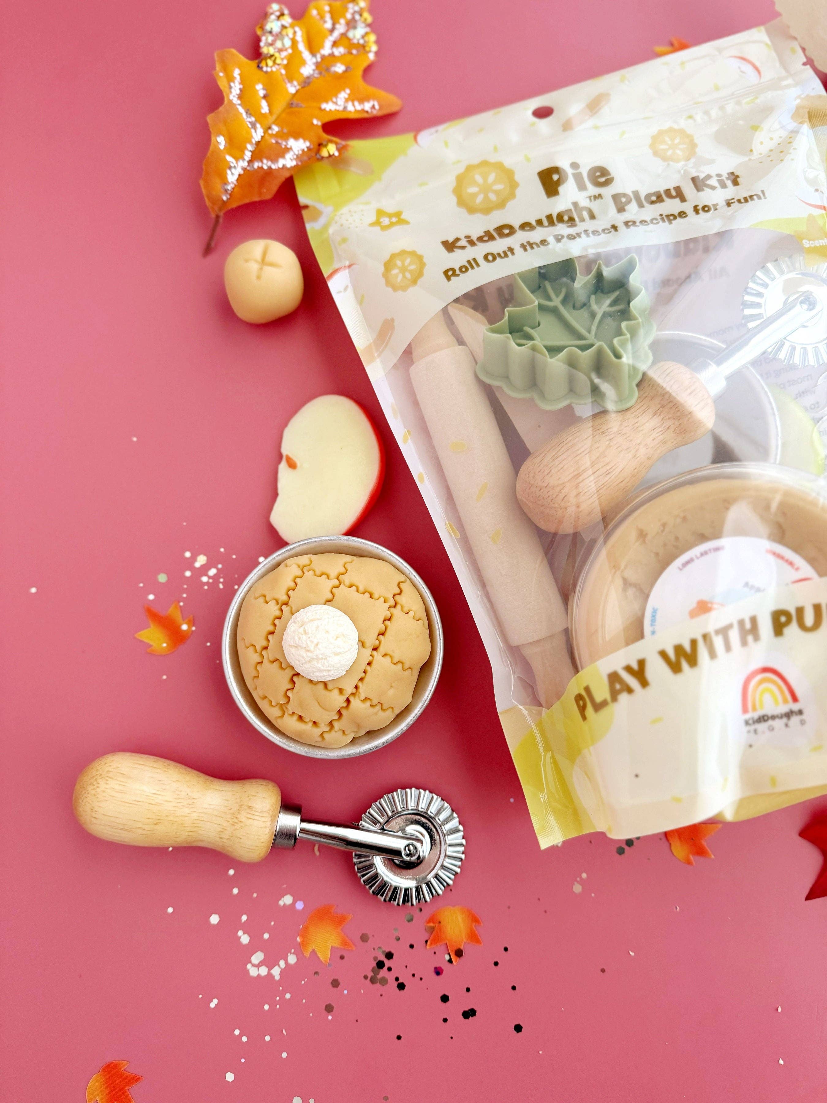 Pie-making play kit with dough, apples, and a rolling pin on a pink background