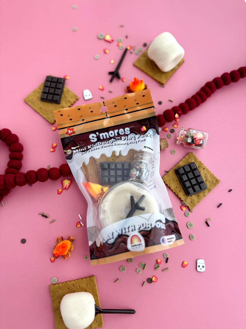 S'mores themed product packaging on a pink background with marshmallows and graham crackers.