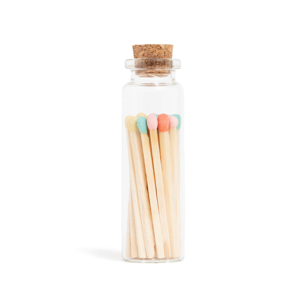 Glass bottle with cork lid containing colorful matchsticks on a white background