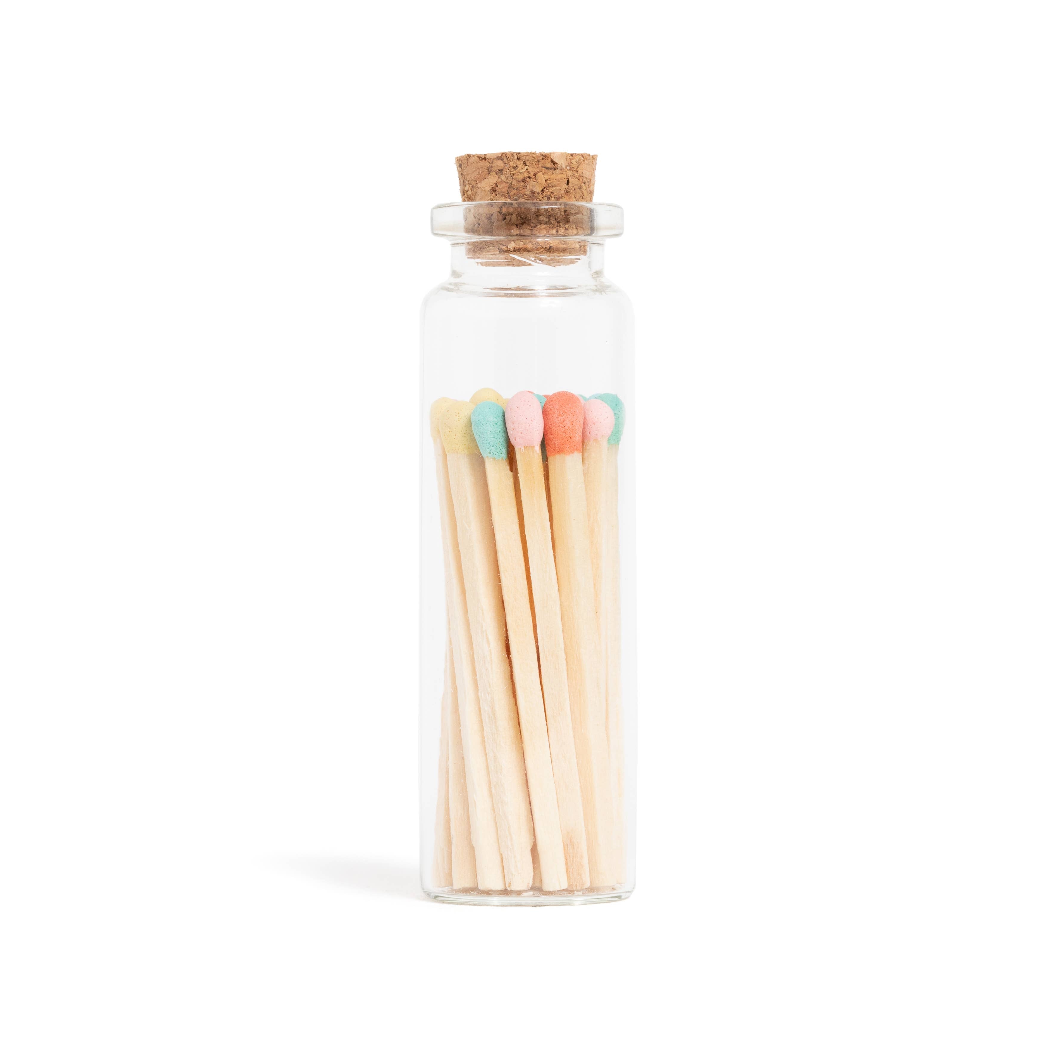Glass bottle with cork lid containing colorful matchsticks on a white background