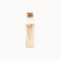 A small clear glass bottle with a cork stopper containing wooden matches with pastel-colored tips, centered on a plain white background.