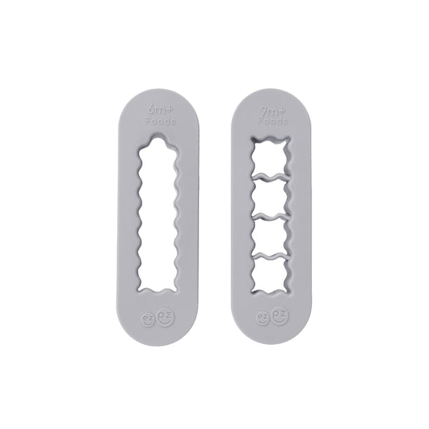 Two gray silicone food cutters designed for baby-led weaning, one for creating finger-length strips and the other for bite-sized cubes.