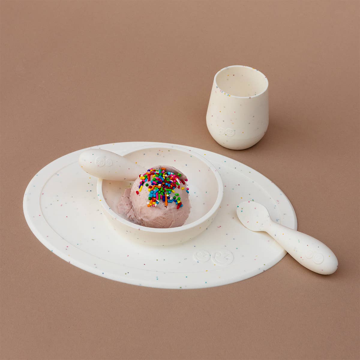 Set of ceramic tableware including a bowl with ice cream, a cup, and a spoon on a brown background