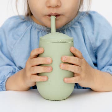 Child drinking from a light green sippy cup with a straw on a white background