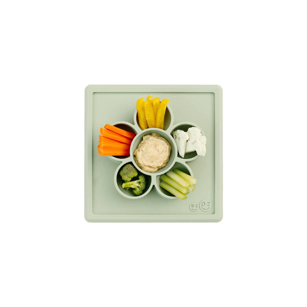 Plastic snack tray with compartments filled with various vegetables and hummus on a white background