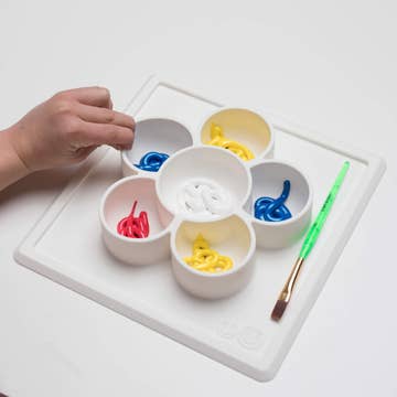 White ceramic paint palette with colorful paint and a brush on a white surface