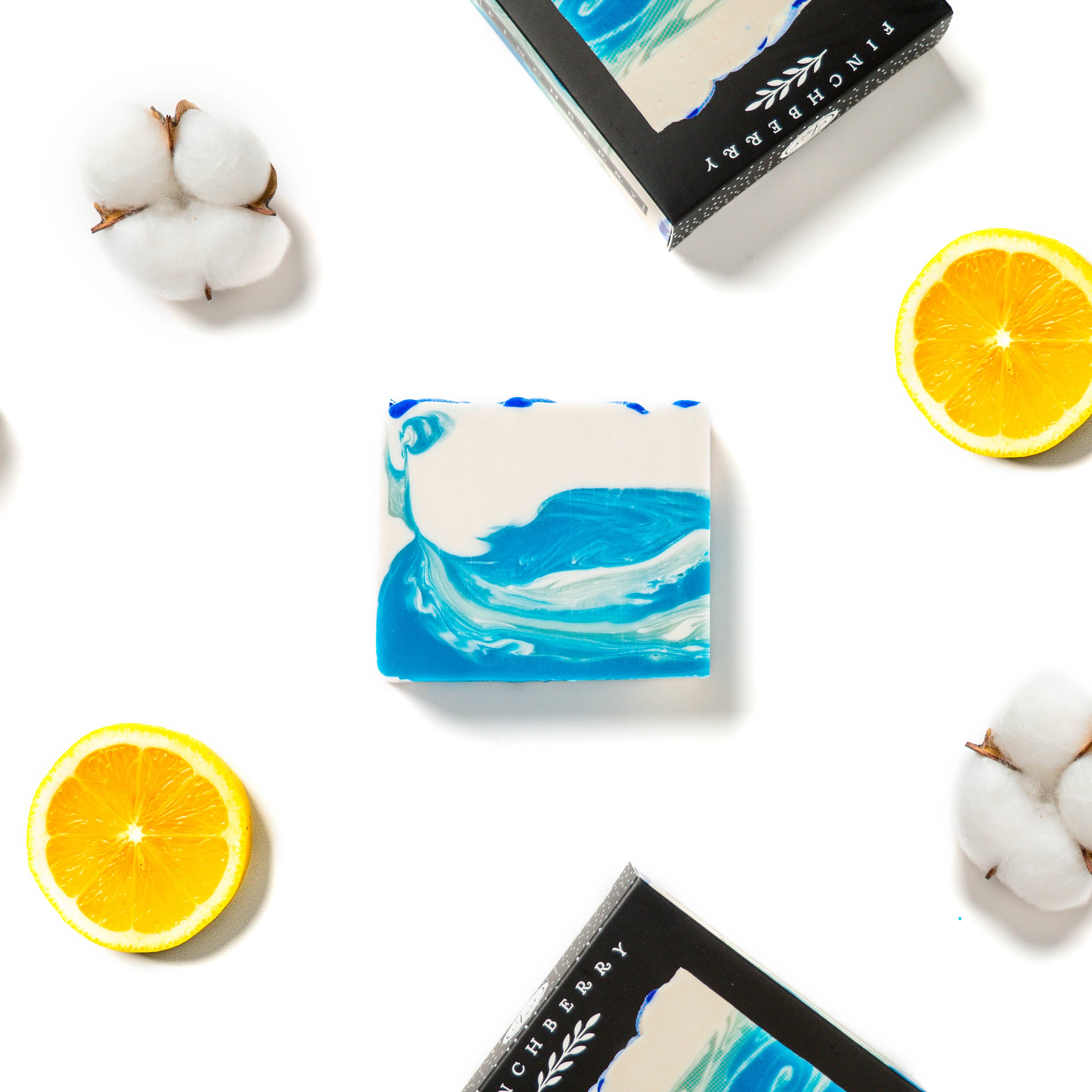 Bar of soap with blue wave design on a white background with oranges and cotton.