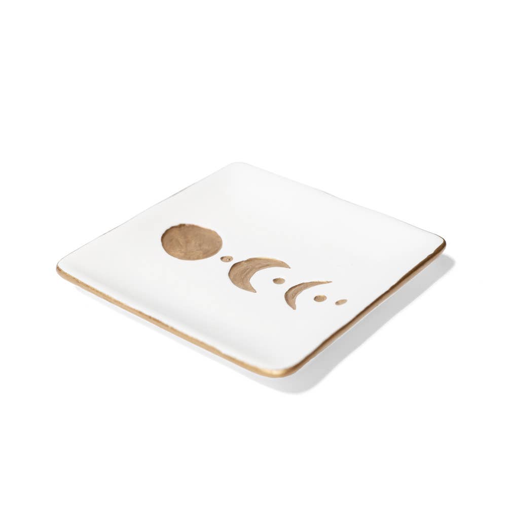 A square white ceramic coaster with a gold-toned metallic rim and a minimalist gold moon phase design on the top surface, shown on a clean white background.