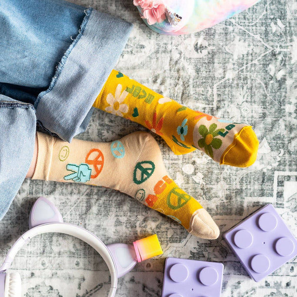 Colorful socks with peace signs and flowers on a textured surface with toys and a mug.