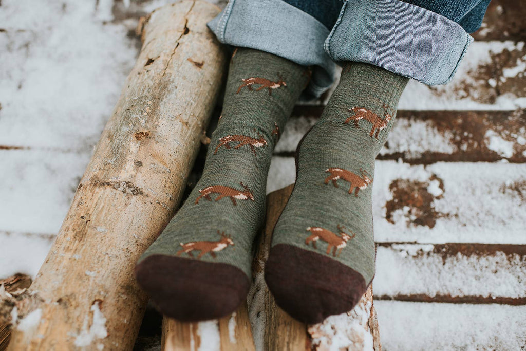 Green socks with deer pattern worn by a person sitting on a log in a snowy setting