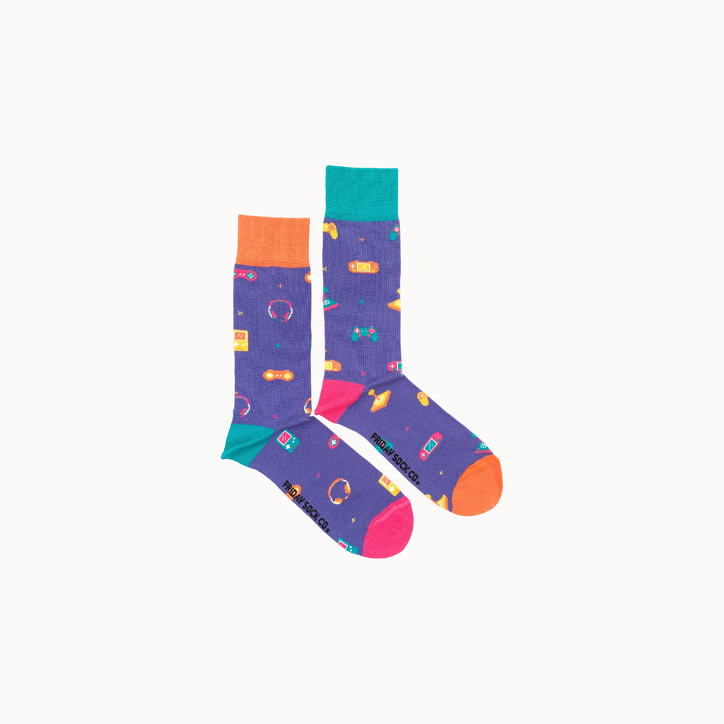 A pair of purple crew socks with a colorful retro video game pattern, featuring orange, teal, and pink accents on the cuffs, heels, and toes, displayed against a plain off-white background.
