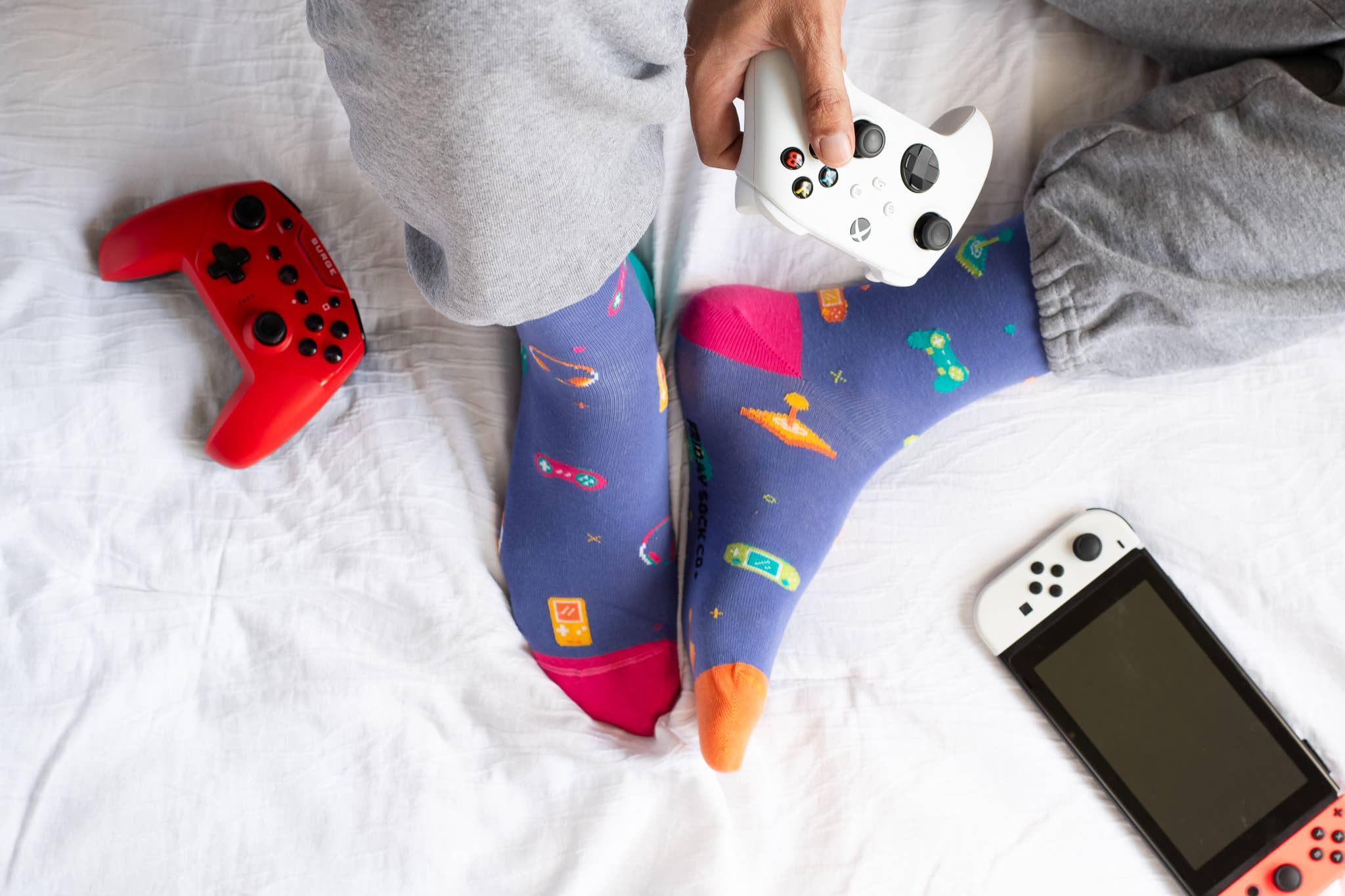 Colorful socks with a moon design, gaming controllers, and a phone on a bed.