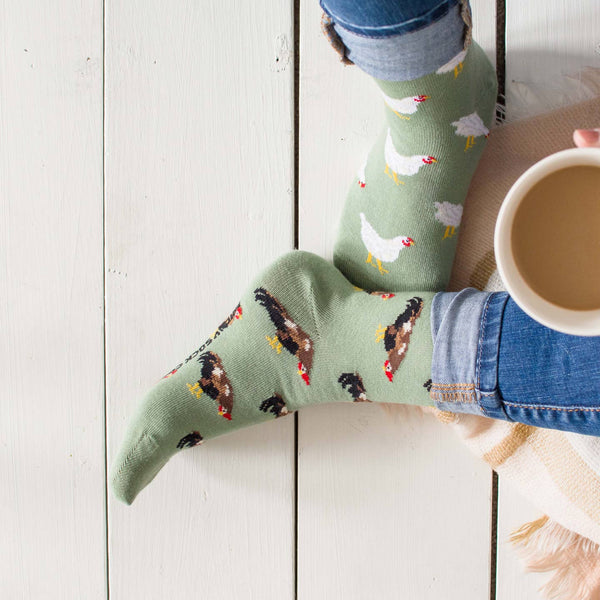 Person wearing socks with animal patterns, sitting on a white surface holding a cup.