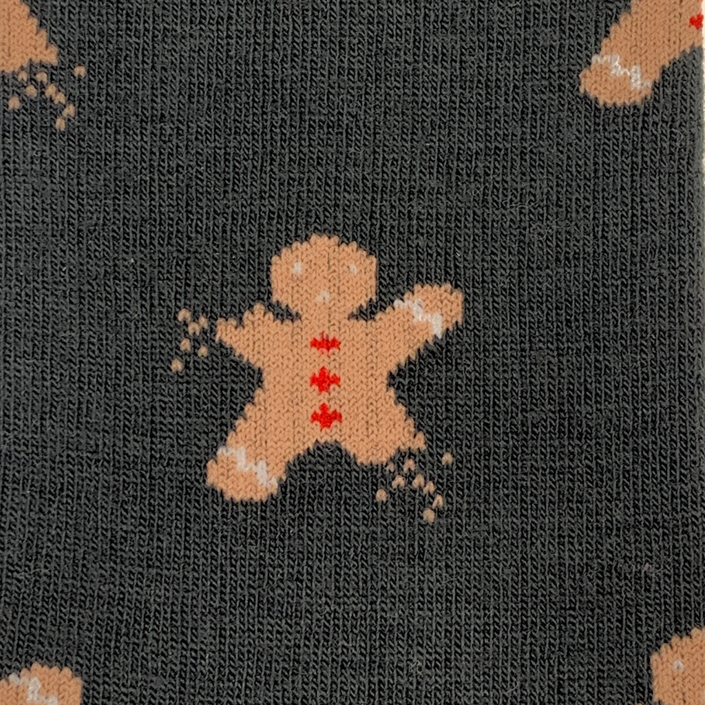 Close-up of a knit fabric with a dark charcoal background and a repeating gingerbread man pattern in tan, with small red buttons and white speckles.