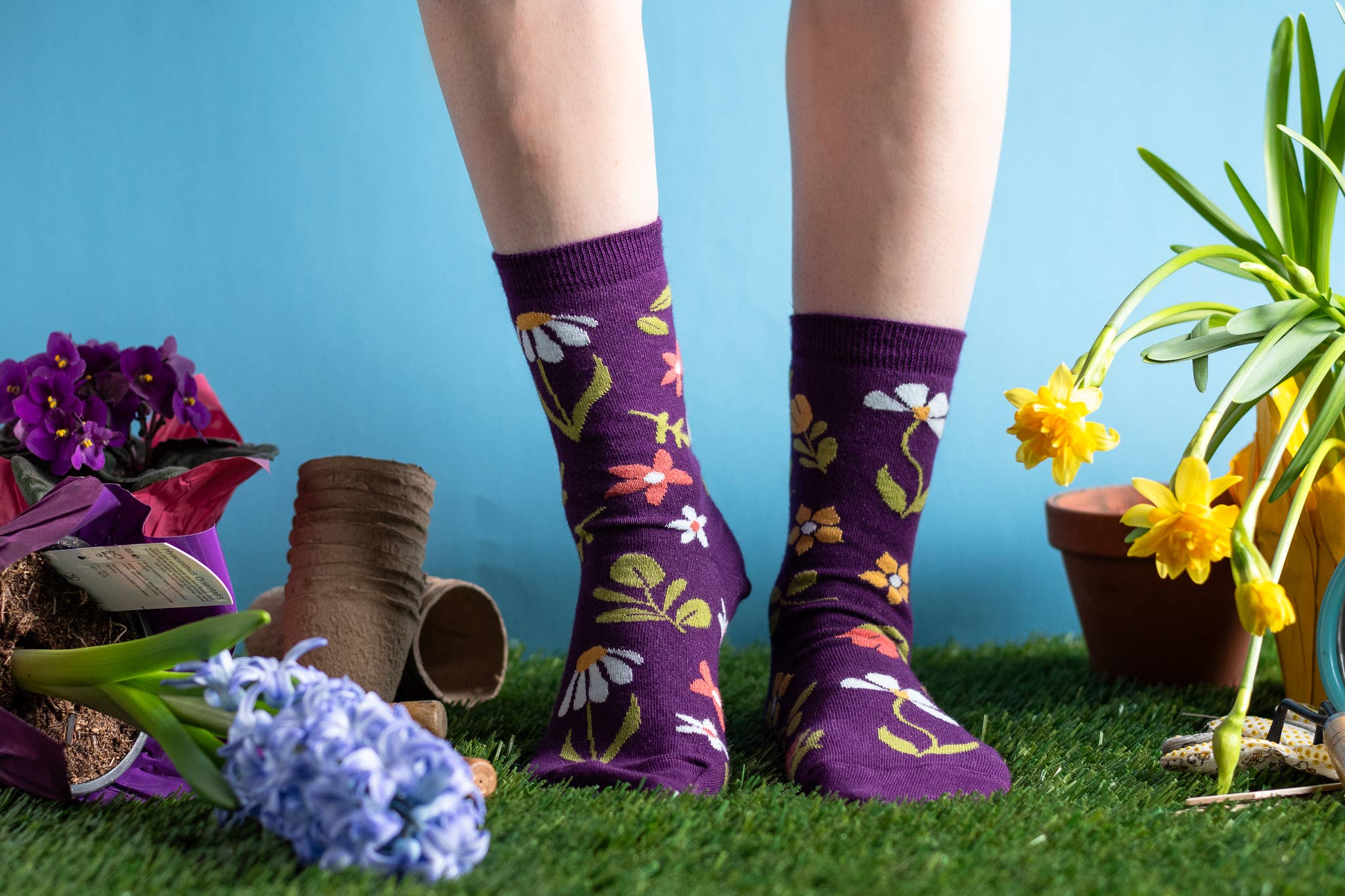 Purple floral-patterned socks worn by a person on grass with plants and flowers.
