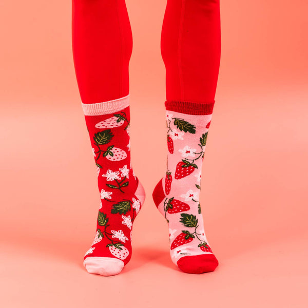 Red socks with strawberry pattern worn on a pink background