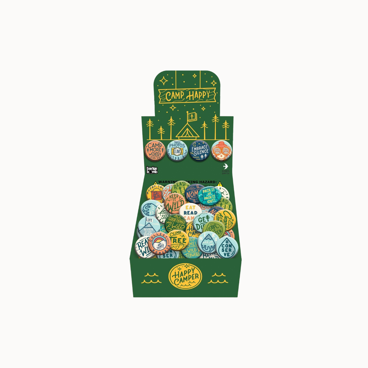 A green cardboard retail display box filled with small round button pins. The display features camping-themed illustrations and the words 'CAMP HAPPY' on the top panel and front.