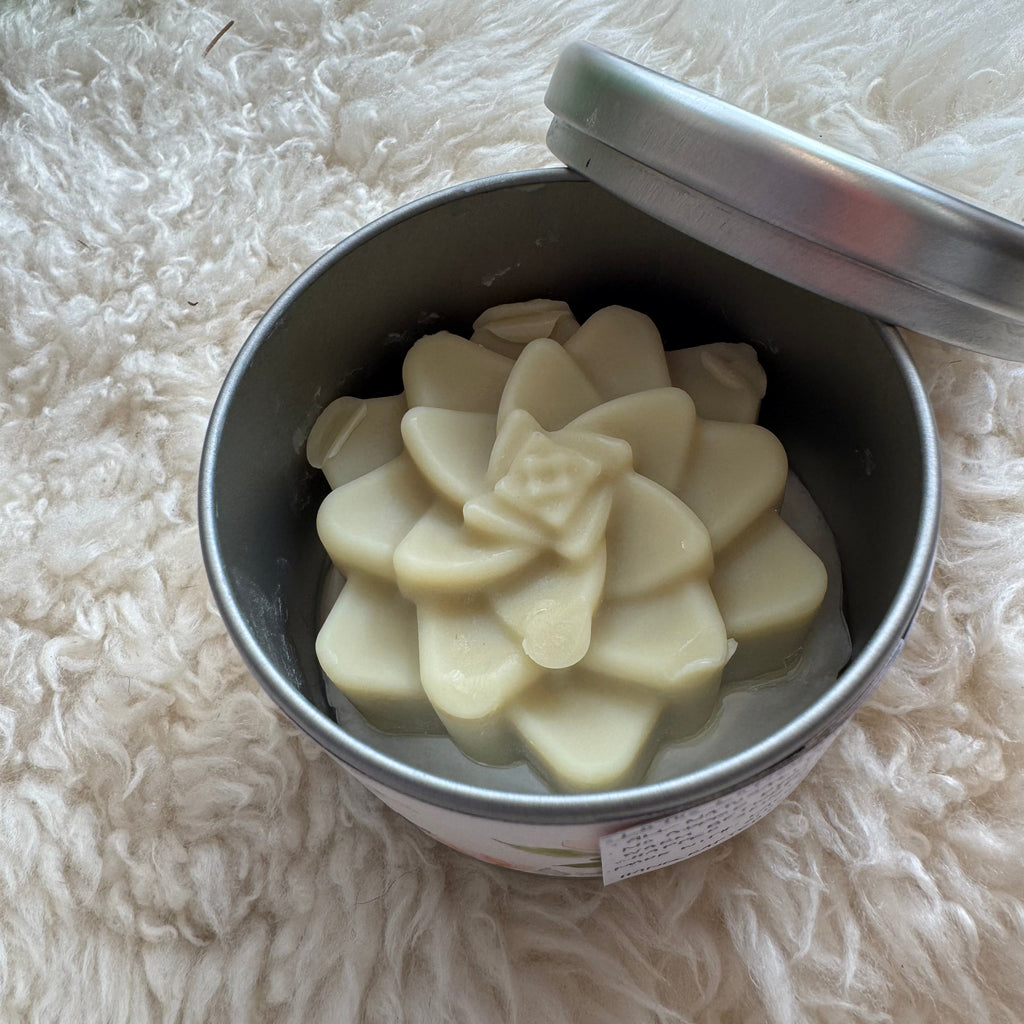 Metal container with white flower-shaped lotion bar on a fluffy white surface