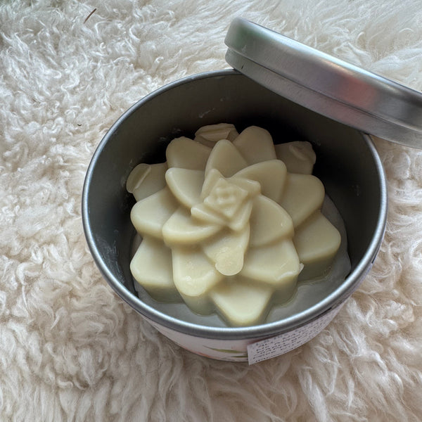 Metal container with white flower-shaped lotion bar on a fluffy white surface