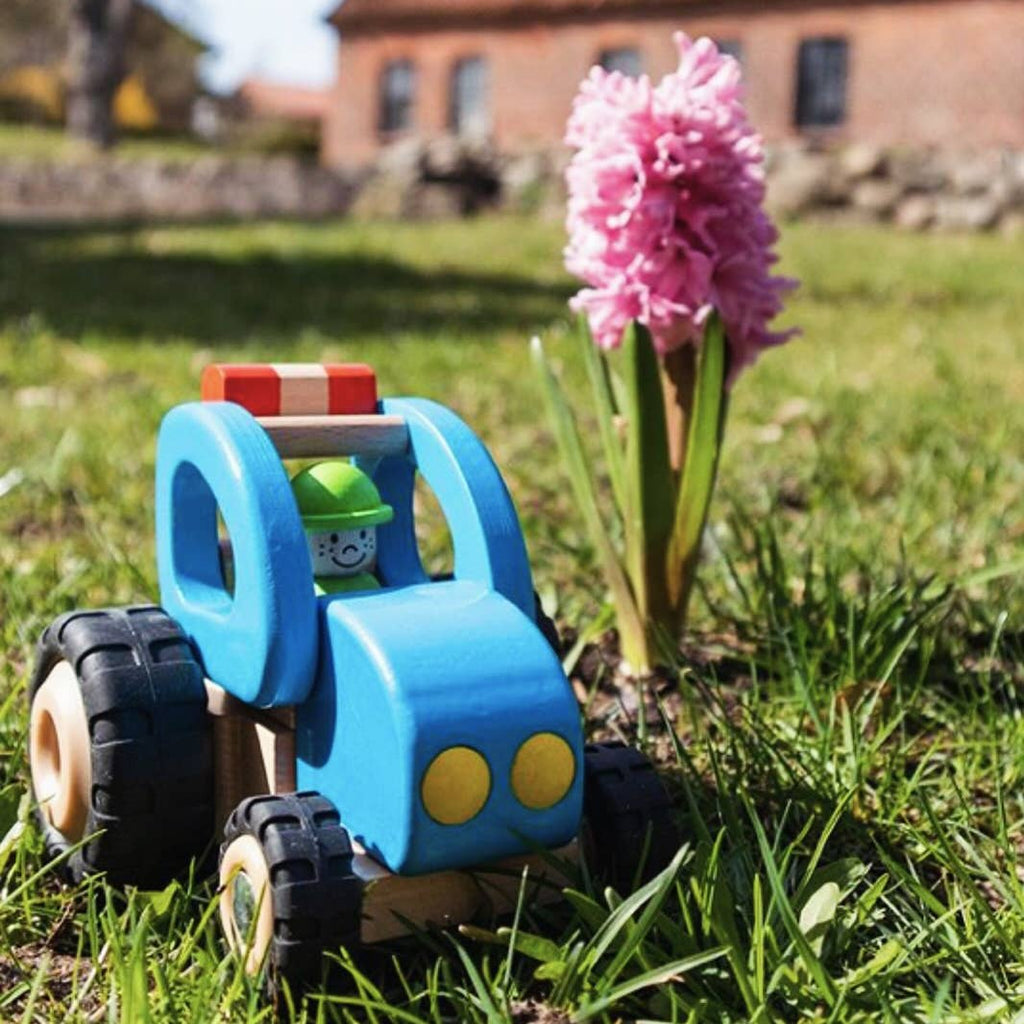 Toy tractor on grass with a pink flower in the foreground