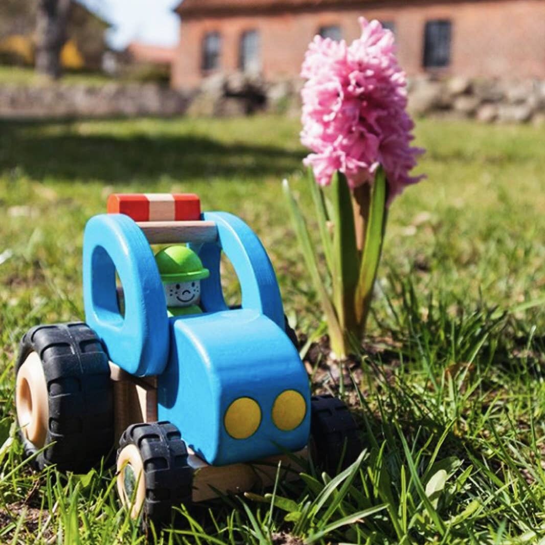 Toy tractor on grass with a pink flower in the foreground