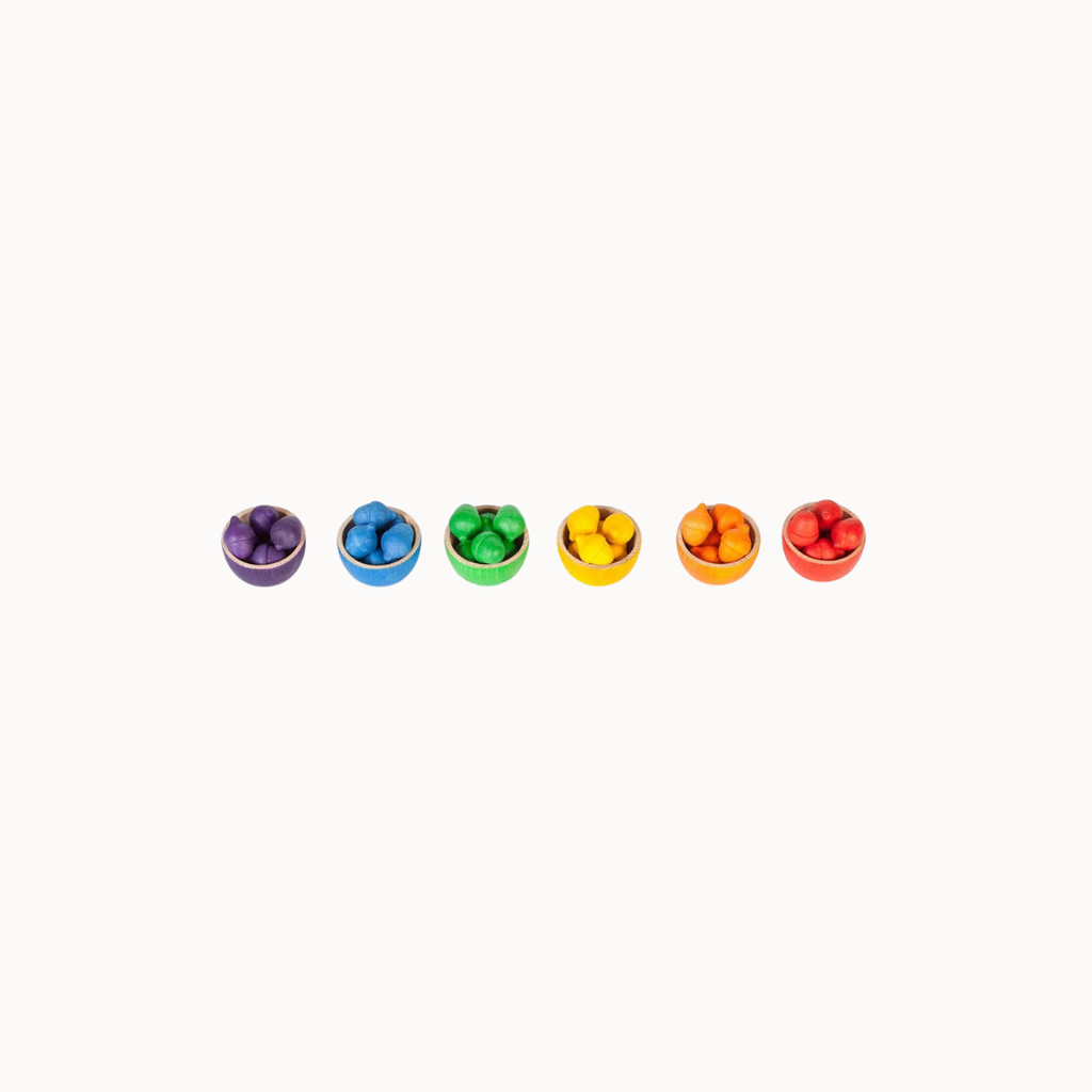 Six small round bowls arranged in a row on a plain white background, each filled with colorful round candies in purple, blue, green, yellow, orange, and red.