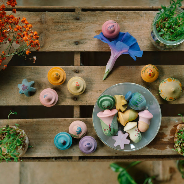 Colorful wooden flower toys on a wooden surface with plants around