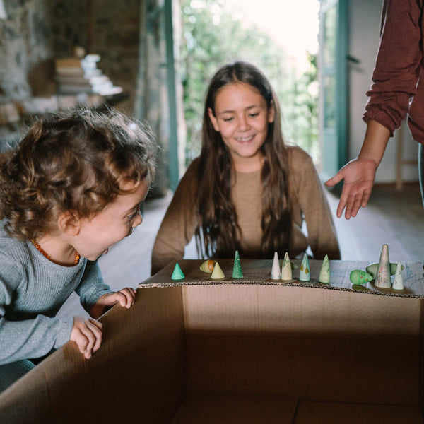 Two children playing with a toy setup on a cardboard box in a home setting.