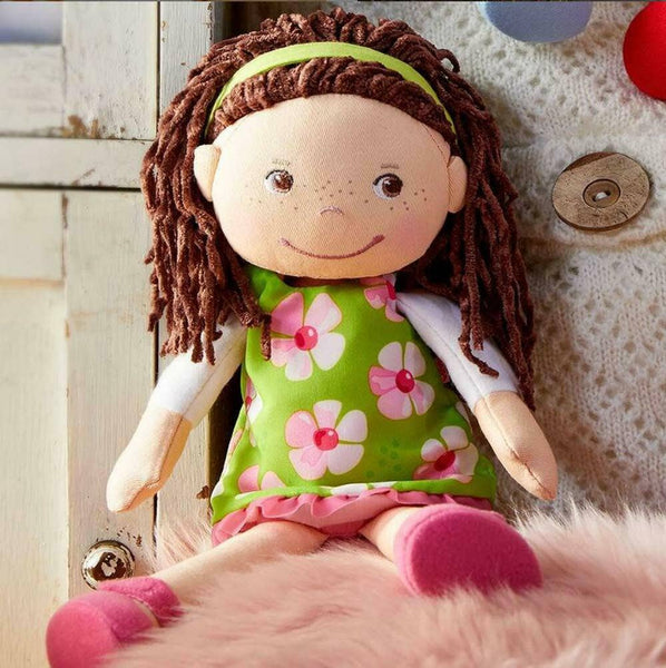 Toy doll with brown hair and a green dress with floral patterns on a textured surface.
