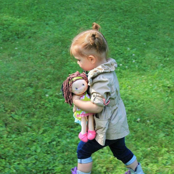 Child holding a doll in a grassy field
