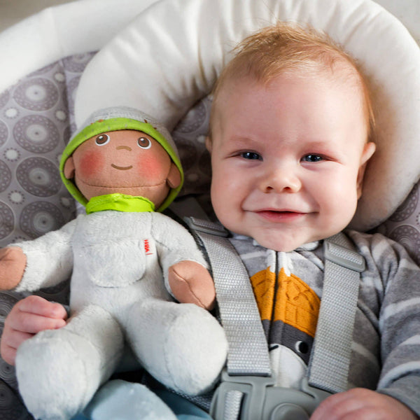 Baby lying in a car seat with a soft toy, smiling at the camera.