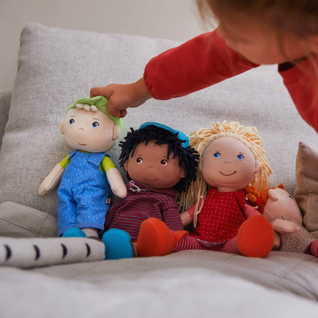 Children's dolls with different hair colors and outfits on a couch, with a child's hand reaching out.