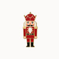 A nutcracker-shaped enamel pin with a red uniform, gold trim, white beard, and black boots on a plain white background.