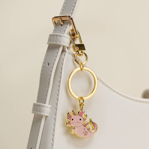 Pink axolotl keychain attached to a white strap with a beige background