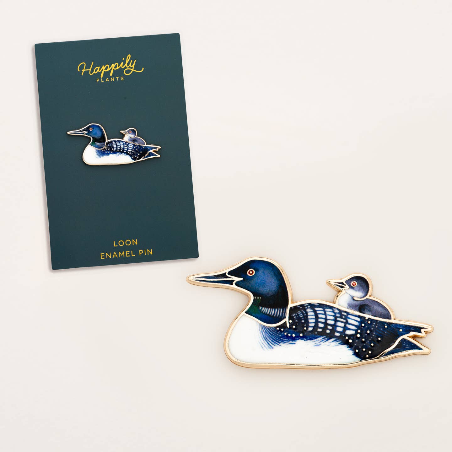 Loon enamel pin on a white background with a card displaying the brand 'Happily Plants'.