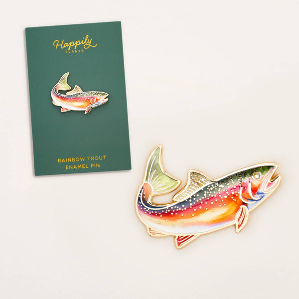 Rainbow trout enamel pin next to a green card with 'Happily Plants' branding on a white background