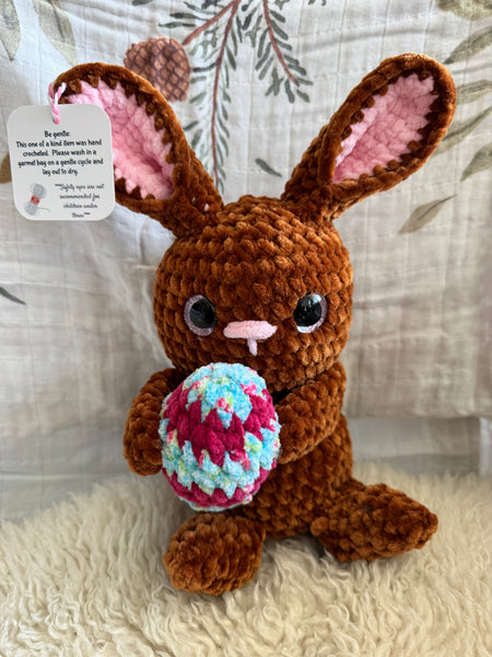 Brown crocheted bunny with a colorful easter egg on a textured surface